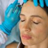 Mulher com o olho fechado enquanto uma médica aplica botox na testa dela.