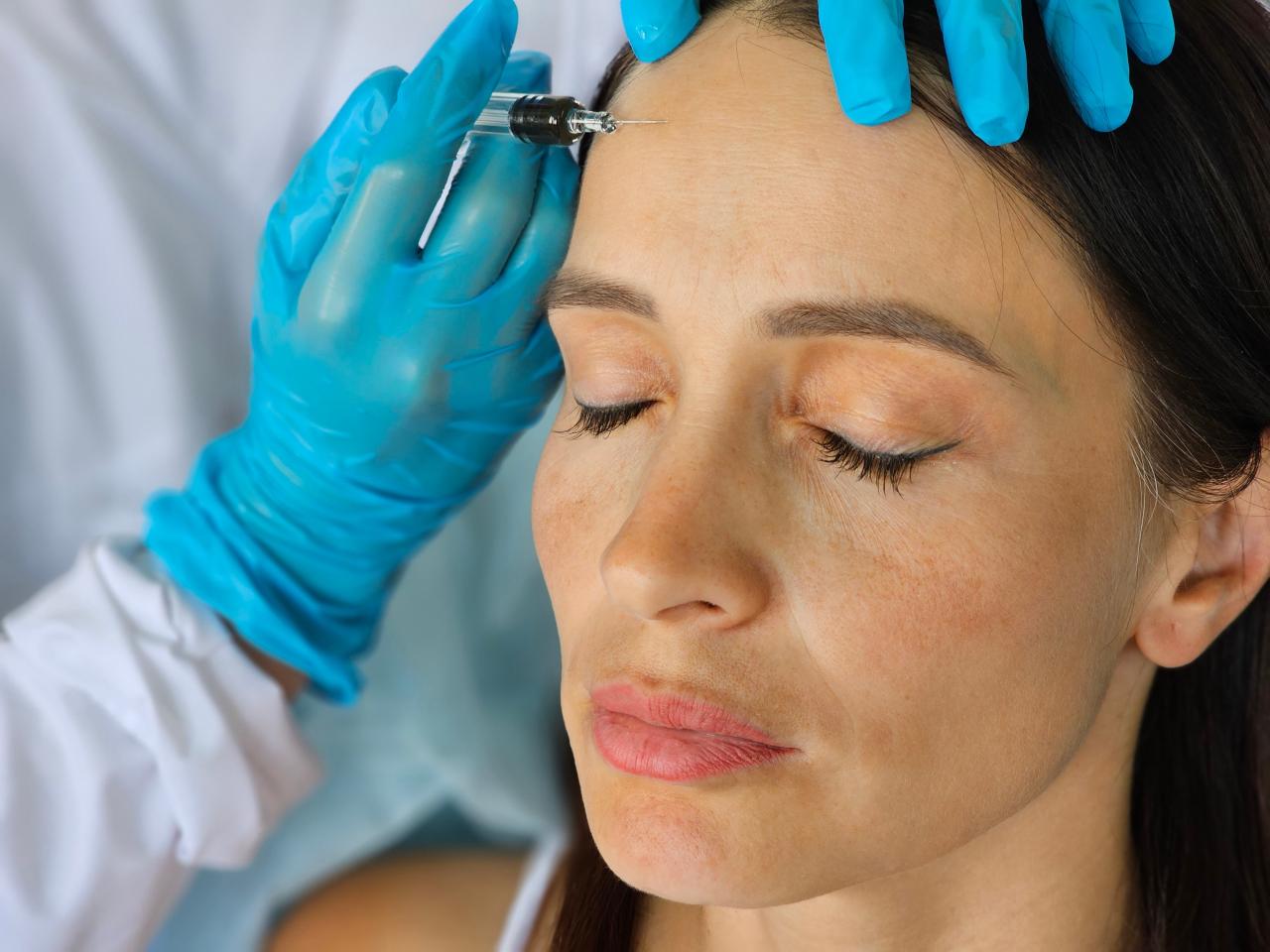 Mulher com o olho fechado enquanto uma médica aplica botox na testa dela.