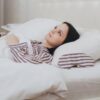 Foto mostra uma mulher deitada na cama acordada, sem conseguir dormir.