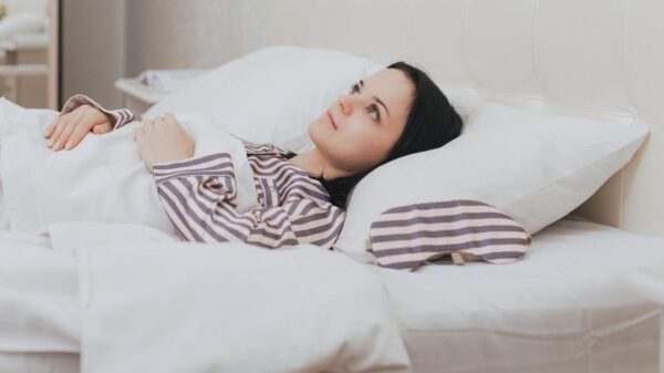 Foto mostra uma mulher deitada na cama acordada, sem conseguir dormir.