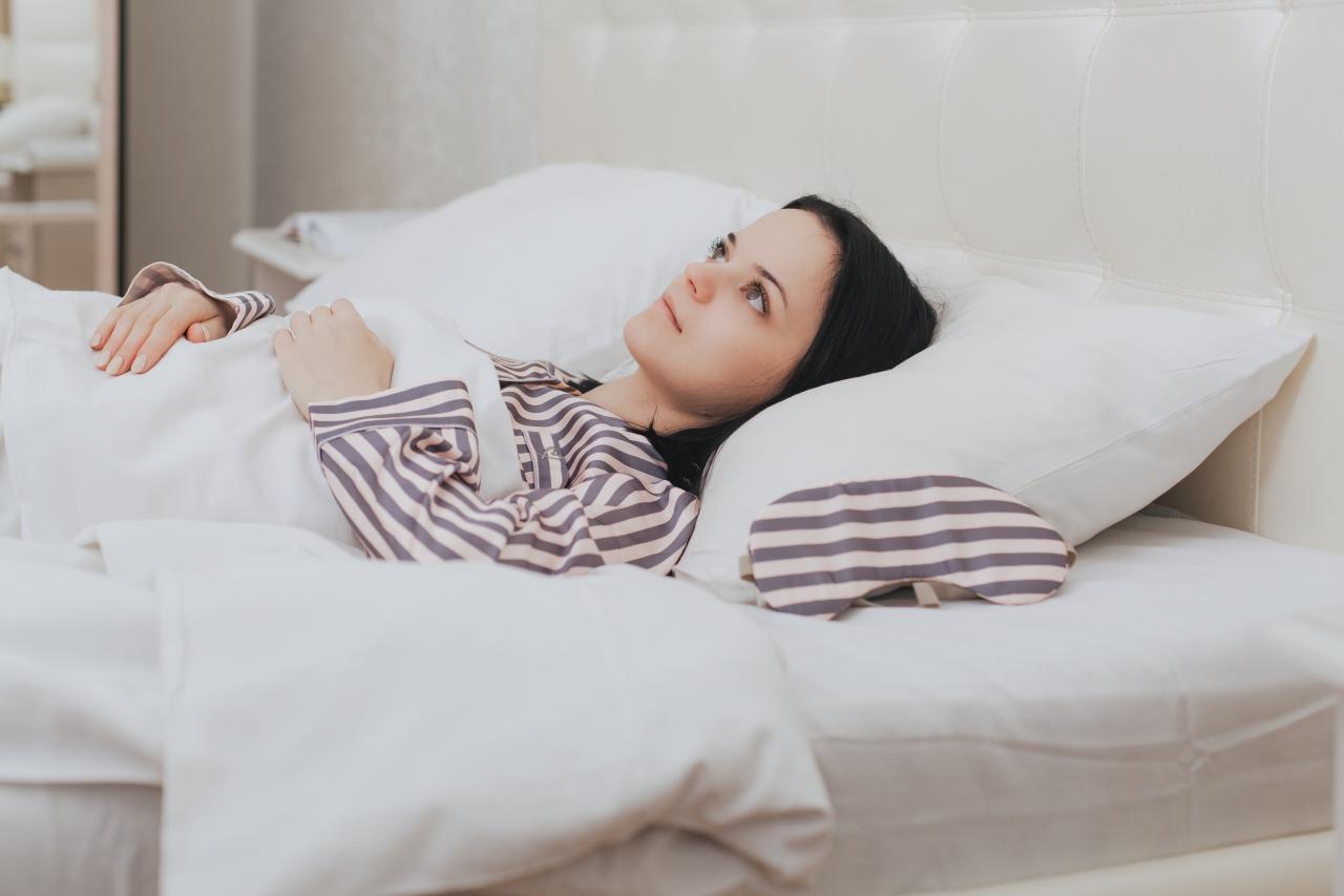 Foto mostra uma mulher deitada na cama acordada, sem conseguir dormir.
