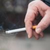 Mão de uma pessoa segurando um cigarro aceso.
