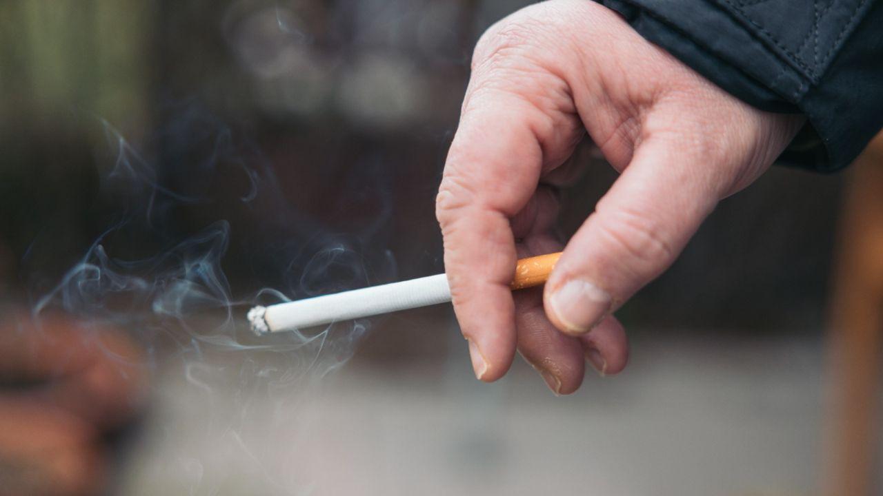 Mão de uma pessoa segurando um cigarro aceso.