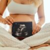 Imagem de uma mulher grávida segurando um ultrassom com imagem na frente da barriga