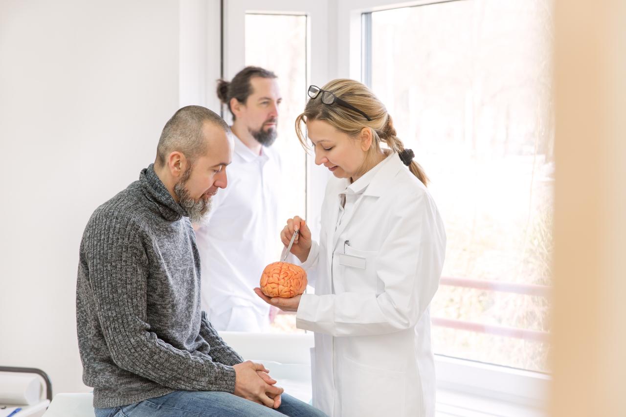 Foto mostra um homem em um consultório médico com uma médica cuidando dele.