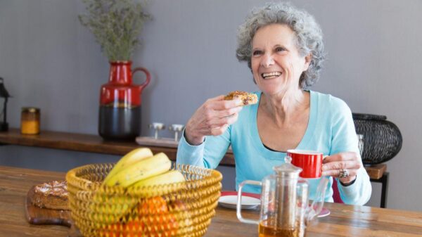 Mulher idosa com cabelo branco sentada em uma mesa com frutas e sorrindo.
