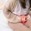 Mulher sentada na cama com dor no útero e um desenho de útero na barriga dela.