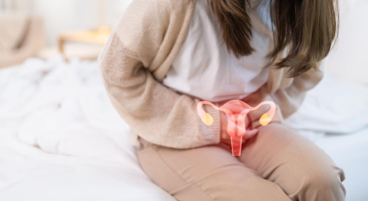 Mulher sentada na cama com dor no útero e um desenho de útero na barriga dela.