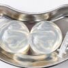 Foto mostra uma plaqueta de alumínio com duas próteses de silicone dentro ao lado de uma injeção.