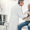 Homem no consultório com um médico o examinando com estetoscópio.
