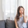 Mulher sentada no sofá com aspecto de dor.