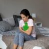 Foto mostra mulher com dor sentada na cama segurando uma bolsa térmica.