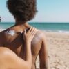 Mulher passando protetor solar em outra mulher na praia.