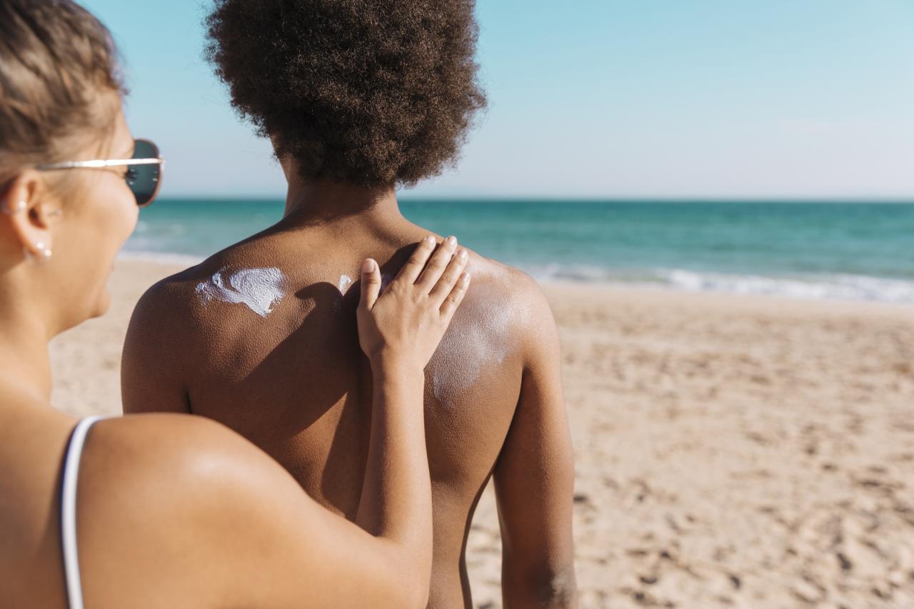 Mulher passando protetor solar em outra mulher na praia.