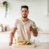 Homem em pé na cozinha com leite em garrafa e outras comidas em cima da bancada da cozinha.