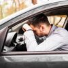 Homem com a cabeça abaixada passando mal dentro do carro.