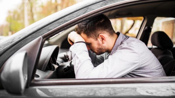 Homem com a cabeça abaixada passando mal dentro do carro.
