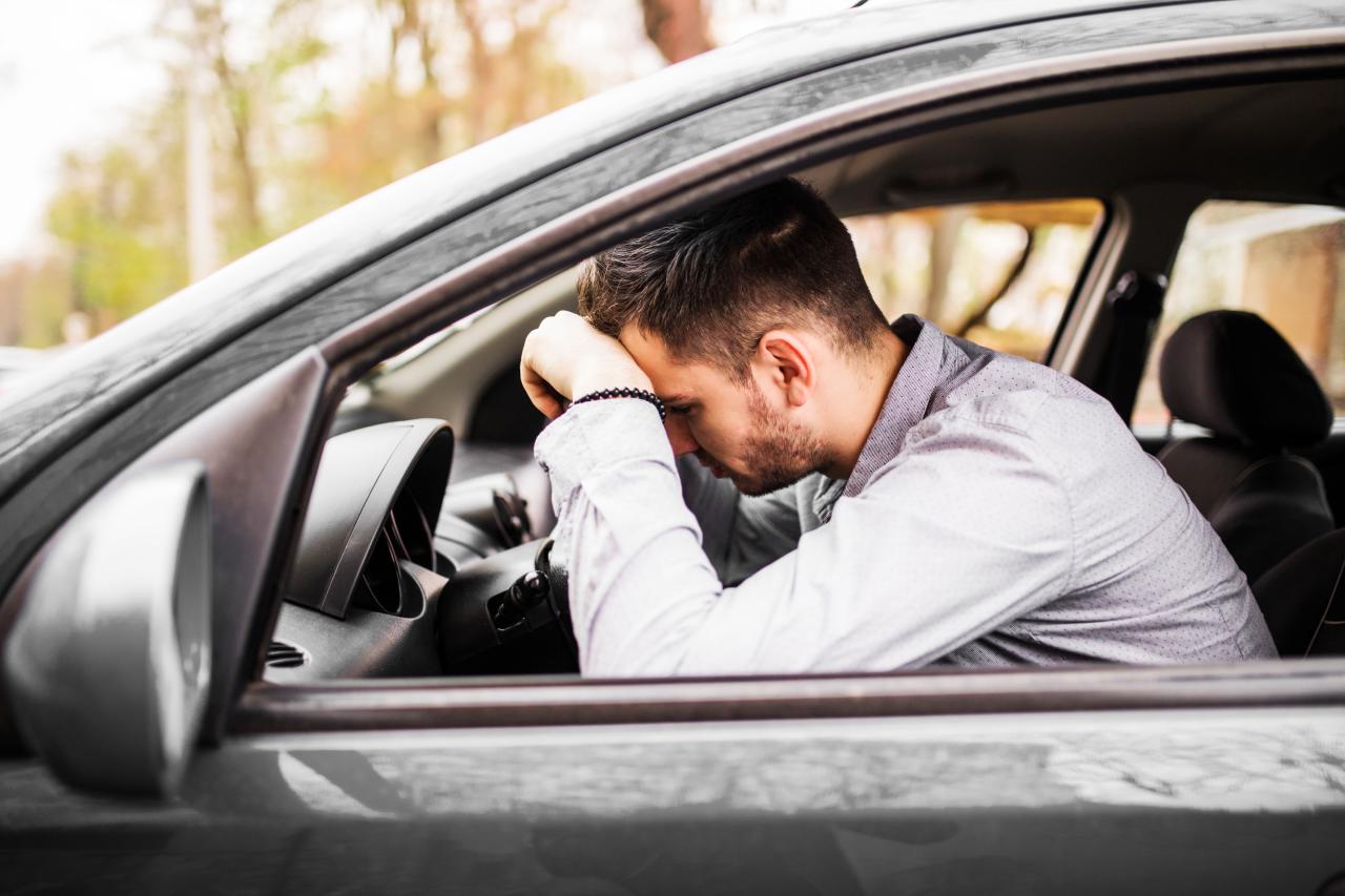 Homem com a cabeça abaixada passando mal dentro do carro.