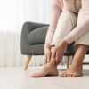 Mulher sentada no sofá com as mãos no tornozelo.