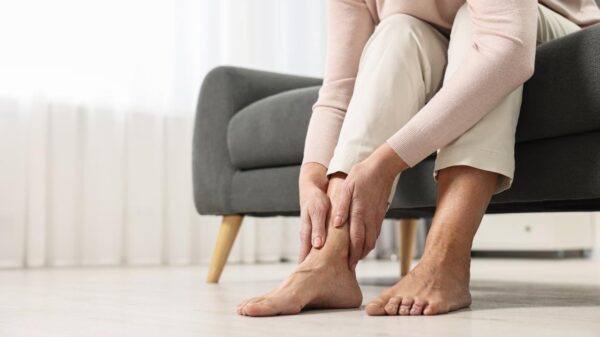 Mulher sentada no sofá com as mãos no tornozelo.