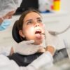 Mulher sentada no consultório do dentista com a boca aberta.