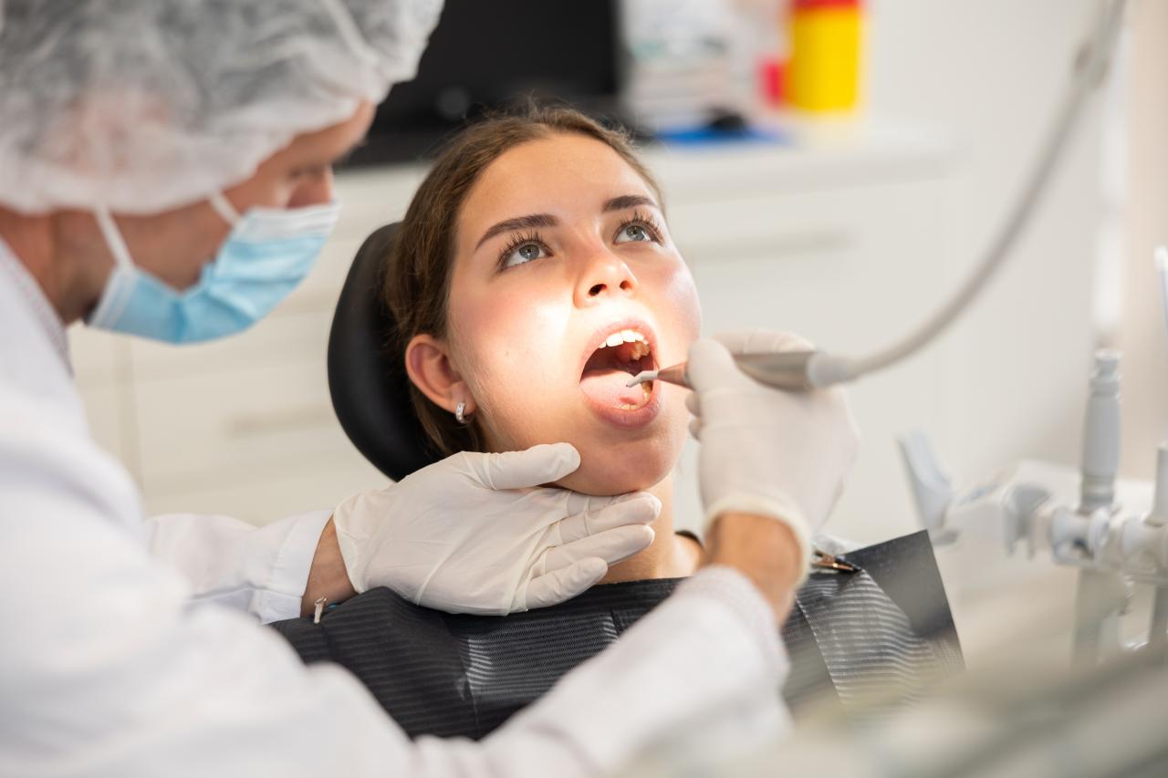 Mulher sentada no consultório do dentista com a boca aberta.