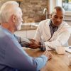 Foto mostra médico conversando com paciente idoso.