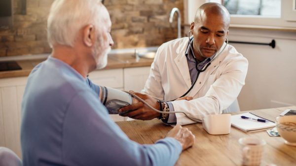 Foto mostra médico conversando com paciente idoso.