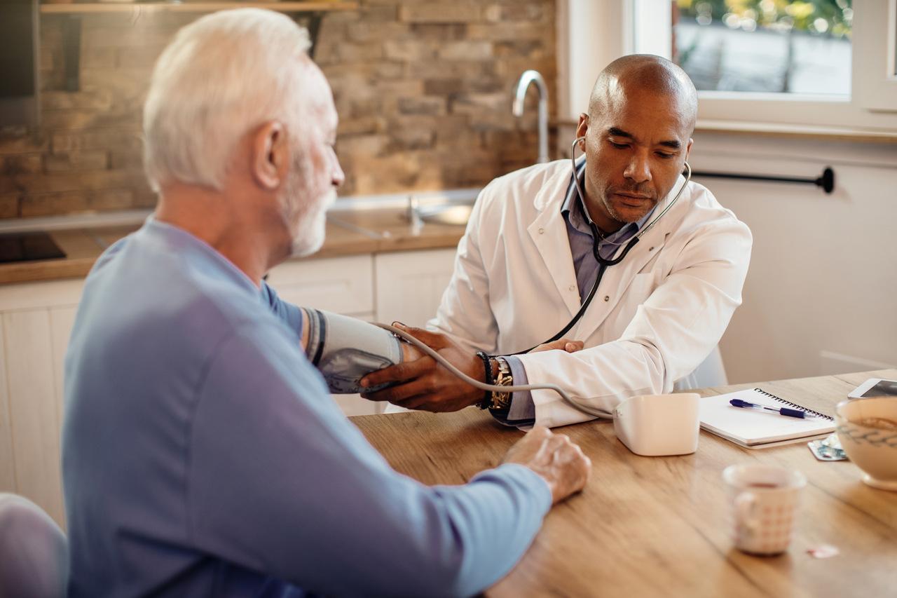 Foto mostra médico conversando com paciente idoso.