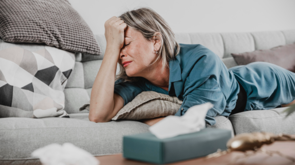 Mulher madura deitada no sofá com semblante preocupado e estressado.